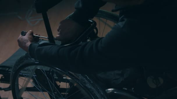 Zijaanzicht van een Amerikaanse mannelijke arbeider in een werkplaats in een fabriek die rolstoelen maakt, op een werkbank zit met handgereedschap en delen van een product monteert, in rolstoelen zit — Stockvideo
