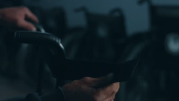 Vista lateral de un trabajador estadounidense en un taller en una fábrica que fabrica sillas de ruedas, sentado en un banco de trabajo usando herramientas de mano y ensamblando partes de un producto, sentado en sillas de ruedas — Vídeo de stock