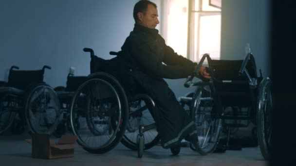 Tekerlekli sandalye üreten, el aletleri kullanan ve bir ürünün parçalarını birleştiren, tekerlekli sandalyede oturan bir fabrikada çalışan Amerikalı erkek işçinin yan görüntüsü. — Stok video