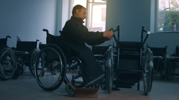 Zijaanzicht van een Amerikaanse mannelijke arbeider in een werkplaats in een fabriek die rolstoelen maakt, op een werkbank zit met handgereedschap en delen van een product monteert, in rolstoelen zit — Stockvideo