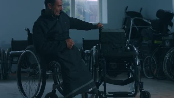 Side view of one American male workers in a workshop at a factory making wheelchairs, sitting at a workbench using hand tools and assembling parts of a product, sitting in wheelchairs — Stock Video