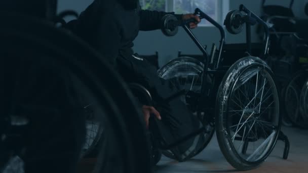Бічний вид на одного американського робітника на фабриці, який виготовляє інвалідні візки, сидить на робочому місці за допомогою ручних інструментів і збирає частини продукту, сидячи в інвалідних візках. — стокове відео