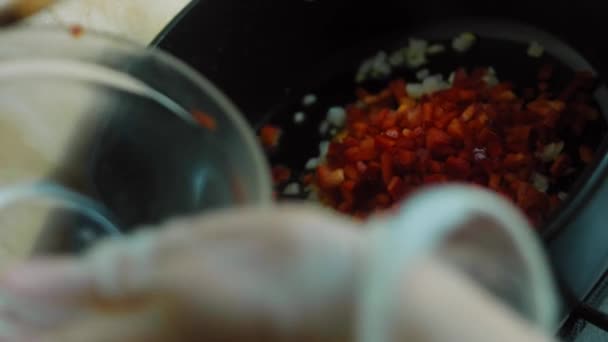 Misture a pimenta vermelha e a cebola pequena na panela com uma colher de madeira — Vídeo de Stock