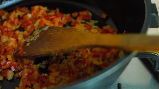 Freír el pimiento rojo y la cebolla pequeña en una sartén con una cuchara de madera — Vídeo de stock