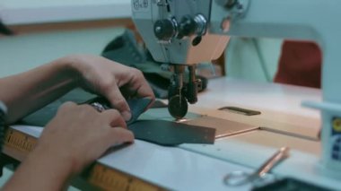 Deri atölyesinde dikiş makinesi çalışıyor. Elleri ayakkabı için deri detaylar üzerinde çalışıyor. Ayakkabı fabrikasında dikiş makinesiyle kadın eli makro çekim.