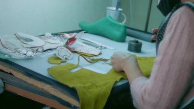 Deri atölyesinde dikiş makinesi çalışıyor. Elleri ayakkabı için deri detaylar üzerinde çalışıyor. Ayakkabı fabrikasında dikiş makinesiyle kadın eli makro çekim.