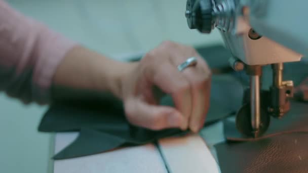 Швейная машина в кожаной мастерской в действии с руками, работающими над кожаными деталями для обуви. Макроснимок женских рук с швейной машинкой на обувной фабрике — стоковое видео