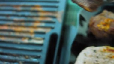 Aşçı ızgaradaki pişmiş eti temizler. Eti diğer taraftaki yemek maşasıyla çevir..