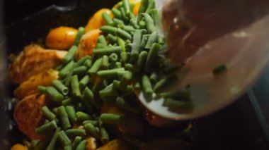 Bal Hardallı Tavuk ve VEGETable tarifi. Pişmiş et ve yeni patatesler tavada. Şef yeşil bezelyeleri yemek maşasıyla hazırlıyor..