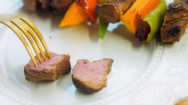 Izgarada sebzeli marine edilmiş sığır kebabı. Şef eti altın çatalla tadıyor. Makro çekim.