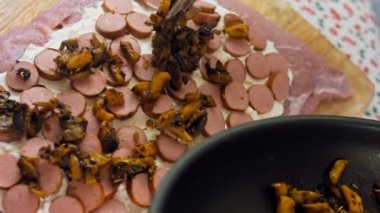 Şef sosis dilimleyicilerini yemek maşasıyla birlikte koyuyor. Şef elmalı mantarları yemek maşasına koyar..