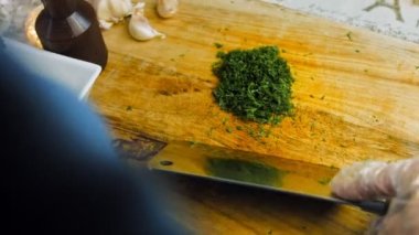 Şef, dilimlenmiş dereotu profesyonel bir bıçakla bir kenara koyar ve maydanozu masaya koyar..