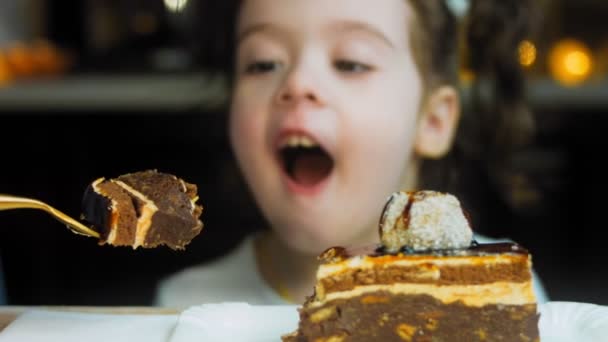チョコレートケーキ コルドン 母親は少女にケーキで金のフォークを与える 女の子はとても面白いです 彼女は彼女の舌で再生し ケーキを待っています — ストック動画