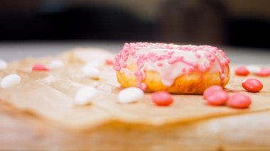 Pembe kremayla süslenmiş pembe çörekler. Çörekler şekerle süslenmiş bir kağıt parçasının üzerinde. Makro ve kaydırma atışı. Şekerler ağır çekimde hareket ediyor. Fırın ve yemek konsepti. Çeşitli renkli çörekler.