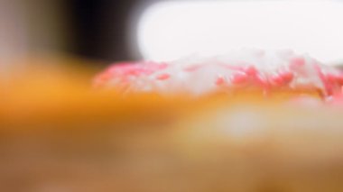 Pembe kremayla süslenmiş pembe çörekler. Çörekler şekerle süslenmiş bir kağıt parçasının üzerinde. Makro ve kaydırma atışı. Şekerler ağır çekimde hareket ediyor. Fırın ve yemek konsepti. Çeşitli renkli çörekler.