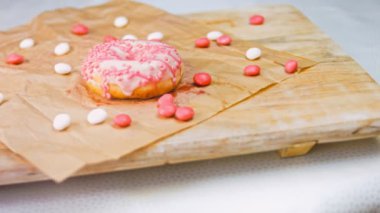 Pembe kremayla süslenmiş pembe çörekler. Çörekler şekerle süslenmiş bir kağıt parçasının üzerinde. Makro ve kaydırma atışı. Şekerler ağır çekimde hareket ediyor. Fırın ve yemek konsepti. Çeşitli renkli çörekler.