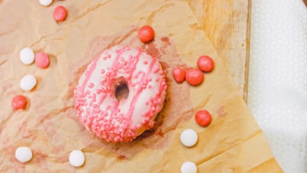 粉红甜甜圈装饰着粉红的糖霜 甜甜圈在用糖果装饰的一张纸上 宏观和滑翔机射击 糖果是慢动作的 面包店和食品概念 各种色彩艳丽的甜甜圈 — 图库视频影像