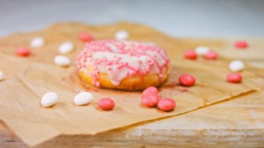 Pembe kremayla süslenmiş pembe çörekler. Çörekler şekerle süslenmiş bir kağıt parçasının üzerinde. Makro ve kaydırma atışı. Şekerler ağır çekimde hareket ediyor. Fırın ve yemek konsepti. Çeşitli renkli çörekler.