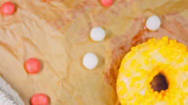 Sarı kremayla süslenmiş pembe çörekler. Çörekler şekerle süslenmiş bir kağıt parçasının üzerinde. Makro ve kaydırma atışı. Şekerler ağır çekimde hareket eder..