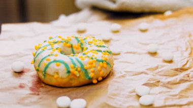 Mavi kremayla süslenmiş sarı çörekler. Çörekler şekerle süslenmiş bir kağıt parçasının üzerinde. Makro ve kaydırma atışı. Makro ve kaydırma atışı. Şekerler ağır çekimde hareket ediyor. Fırın ve yemek.