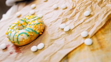 Mavi kremayla süslenmiş sarı çörekler. Çörekler şekerle süslenmiş bir kağıt parçasının üzerinde. Makro ve kaydırma atışı. Makro ve kaydırma atışı. Şekerler ağır çekimde hareket ediyor. Fırın ve yemek.