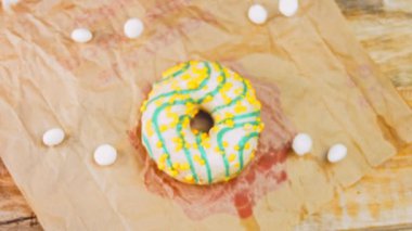 Mavi kremayla süslenmiş sarı çörekler. Çörekler şekerle süslenmiş bir kağıt parçasının üzerinde. Makro ve kaydırma atışı. Makro ve kaydırma atışı. Şekerler ağır çekimde hareket ediyor. Fırın ve yemek.