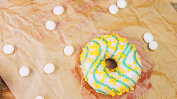 黄色的甜甜圈装饰着蓝色的糖霜 甜甜圈在用糖果装饰的一张纸上 宏观和滑翔机射击 宏观和滑翔机射击 糖果是慢动作的 面包店和食品 — 图库视频影像
