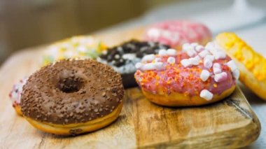 Çikolata, marşmelov ve retro pişirme tepsisindeki şekerli çörekler. Donutlar doğal çikolatayla süslenmiş bir kağıdın üzerinde. Makro ve kaydırma atışı. Çeşitli renkli çörekler. Çikolata, pembe, mavi çörekler