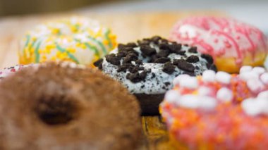 Çikolata, marşmelov ve retro pişirme tepsisindeki şekerli çörekler. Donutlar doğal çikolatayla süslenmiş bir kağıdın üzerinde. Makro ve kaydırma atışı. Çeşitli renkli çörekler. Çikolata, pembe, mavi çörekler