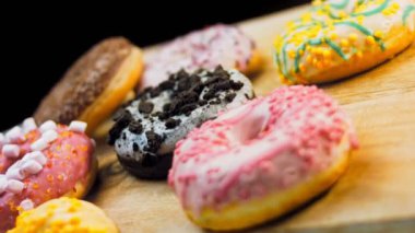 Çikolata, marşmelov ve retro pişirme tepsisindeki şekerli çörekler. Donutlar doğal çikolatayla süslenmiş bir kağıdın üzerinde. Makro ve kaydırma atışı. Çeşitli renkli çörekler. Çikolata, pembe, mavi çörekler