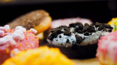 Çikolata, marşmelov ve retro pişirme tepsisindeki şekerli çörekler. Donutlar doğal çikolatayla süslenmiş bir kağıdın üzerinde. Makro ve kaydırma atışı. Çeşitli renkli çörekler. Çikolata, pembe, mavi çörekler