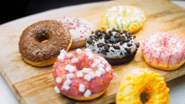 Çikolata, marşmelov ve retro pişirme tepsisindeki şekerli çörekler. Donutlar doğal çikolatayla süslenmiş bir kağıdın üzerinde. Makro ve kaydırma atışı. Çeşitli renkli çörekler. Çikolata, pembe, mavi çörekler