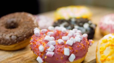 Çikolata, marşmelov ve retro pişirme tepsisindeki şekerli çörekler. Donutlar doğal çikolatayla süslenmiş bir kağıdın üzerinde. Makro ve kaydırma atışı. Çeşitli renkli çörekler. Çikolata, pembe, mavi çörekler