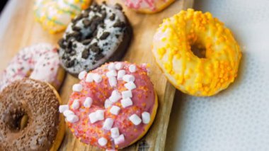 Çikolata, marşmelov ve retro pişirme tepsisindeki şekerli çörekler. Donutlar doğal çikolatayla süslenmiş bir kağıdın üzerinde. Makro ve kaydırma atışı. Çeşitli renkli çörekler. Çikolata, pembe, mavi çörekler