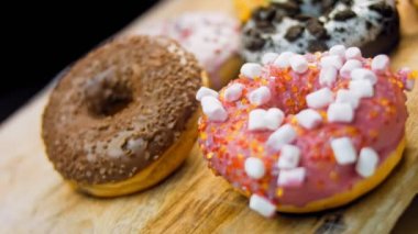 Çikolata, marşmelov ve retro pişirme tepsisindeki şekerli çörekler. Donutlar doğal çikolatayla süslenmiş bir kağıdın üzerinde. Makro ve kaydırma atışı. Çeşitli renkli çörekler. Çikolata, pembe, mavi çörekler