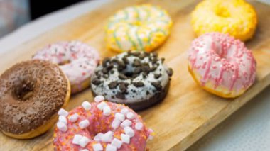 Çikolata, marşmelov ve retro pişirme tepsisindeki şekerli çörekler. Donutlar doğal çikolatayla süslenmiş bir kağıdın üzerinde. Makro ve kaydırma atışı. Çeşitli renkli çörekler. Çikolata, pembe, mavi çörekler