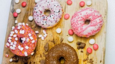 Çikolata, marşmelov ve retro pişirme tepsisindeki şekerli çörekler. Donutlar doğal çikolatayla süslenmiş bir kağıdın üzerinde. Makro ve kaydırma atışı. Çeşitli renkli çörekler. Çikolata, pembe, mavi çörekler