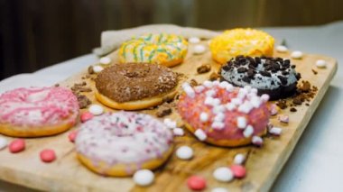 Çikolata, marşmelov ve retro pişirme tepsisindeki şekerli çörekler. Donutlar doğal çikolatayla süslenmiş bir kağıdın üzerinde. Makro ve kaydırma atışı. Çeşitli renkli çörekler. Çikolata, pembe, mavi çörekler