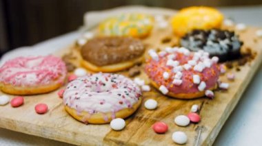 Çikolata, marşmelov ve retro pişirme tepsisindeki şekerli çörekler. Donutlar doğal çikolatayla süslenmiş bir kağıdın üzerinde. Makro ve kaydırma atışı. Çeşitli renkli çörekler. Çikolata, pembe, mavi çörekler
