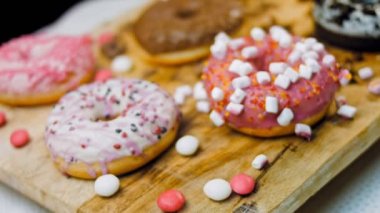 Çikolata, marşmelov ve retro pişirme tepsisindeki şekerli çörekler. Donutlar doğal çikolatayla süslenmiş bir kağıdın üzerinde. Makro ve kaydırma atışı. Çeşitli renkli çörekler. Çikolata, pembe, mavi çörekler
