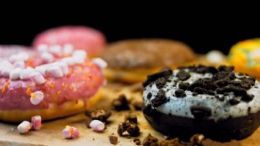 Çikolata, marşmelov ve retro pişirme tepsisindeki şekerli çörekler. Donutlar doğal çikolatayla süslenmiş bir kağıdın üzerinde. Makro ve kaydırma atışı. Çeşitli renkli çörekler. Çikolata, pembe, mavi çörekler