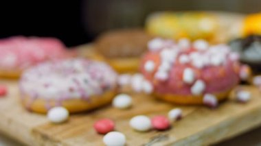 Çikolata, marşmelov ve retro pişirme tepsisindeki şekerli çörekler. Donutlar doğal çikolatayla süslenmiş bir kağıdın üzerinde. Makro ve kaydırma atışı. Çeşitli renkli çörekler. Çikolata, pembe, mavi çörekler