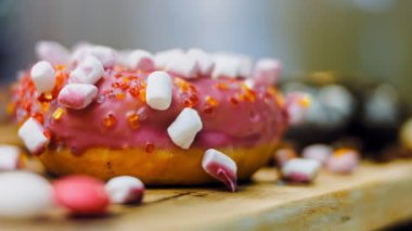 Çikolata, marşmelov ve retro pişirme tepsisindeki şekerli çörekler. Donutlar doğal çikolatayla süslenmiş bir kağıdın üzerinde. Makro ve kaydırma atışı. Çeşitli renkli çörekler. Çikolata, pembe, mavi çörekler