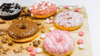Çikolata, marşmelov ve retro pişirme tepsisindeki şekerli çörekler. Donutlar doğal çikolatayla süslenmiş bir kağıdın üzerinde. Makro ve kaydırma atışı. Çeşitli renkli çörekler. Çikolata, pembe, mavi çörekler