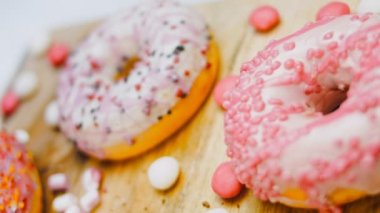 Çikolata, marşmelov ve retro pişirme tepsisindeki şekerli çörekler. Donutlar doğal çikolatayla süslenmiş bir kağıdın üzerinde. Makro ve kaydırma atışı. Çeşitli renkli çörekler. Çikolata, pembe, mavi çörekler