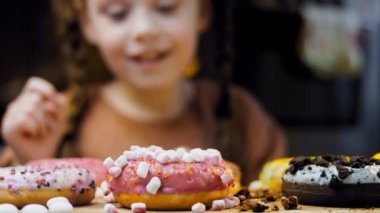 Kız hediyeler arasından seçiyor, parmağını işaret ediyor. Çikolata, marşmelov ve retro pişirme tepsisindeki şekerli çörekler. Donutlar doğal çikolatayla süslenmiş bir kağıdın üzerinde. Makro ve kaydırıcı