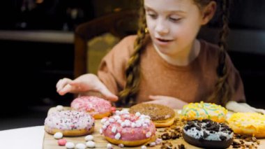 Kız hediyeler arasından seçiyor, parmağını işaret ediyor. Çikolata, marşmelov ve retro pişirme tepsisindeki şekerli çörekler. Donutlar doğal çikolatayla süslenmiş bir kağıdın üzerinde. Makro ve kaydırıcı