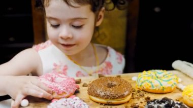 Kız donut yiyor. Çikolata, marşmelov ve retro pişirme tepsisindeki şekerli çörekler. Donutlar doğal çikolatayla süslenmiş bir kağıdın üzerinde. Makro ve kaydırma atışı. Çeşitli renkli çörekler.