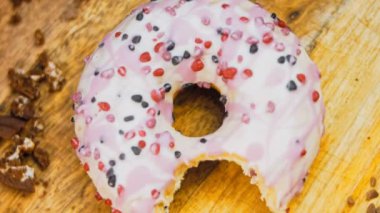 Pembe kremayla süslenmiş pembe çörekler. Çörekler şekerle süslenmiş bir kağıt parçasının üzerinde. Makro ve kaydırma atışı. Şekerler ağır çekimde hareket ediyor. Fırın ve yemek konsepti. Çeşitli renkli çörekler.