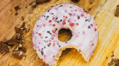 Pembe kremayla süslenmiş pembe çörekler. Çörekler şekerle süslenmiş bir kağıt parçasının üzerinde. Makro ve kaydırma atışı. Şekerler ağır çekimde hareket ediyor. Fırın ve yemek konsepti. Çeşitli renkli çörekler.